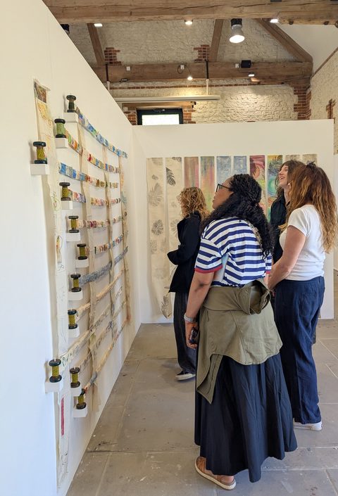 Visitors in the gallery beside the stitched strips mounted on cotton reels